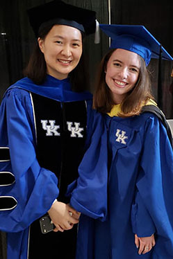 Two people stand in UK graduation gowns