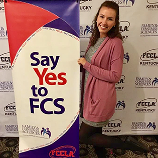 Internship Spotlight: Madison Showalter stands beside a Say Yes to FCS sign